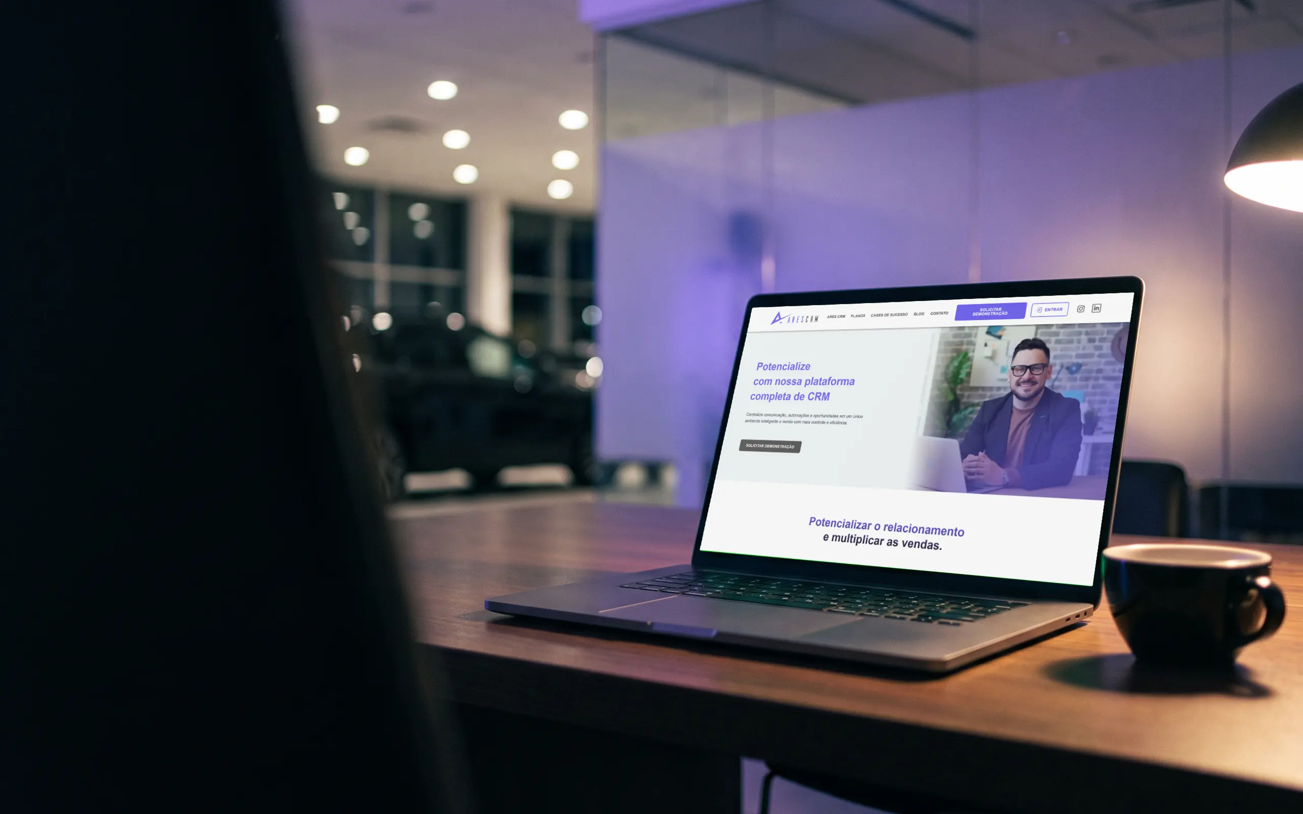 Notebook sobre a mesa de um escritório de concessionária à noite, exibindo o site do Ares CRM